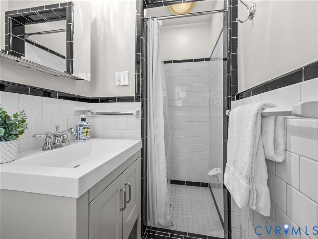 Tiled shower stall with a glass enclosure, white subway tile walls, black accent tiling, and a gray vanity with an integrated sink