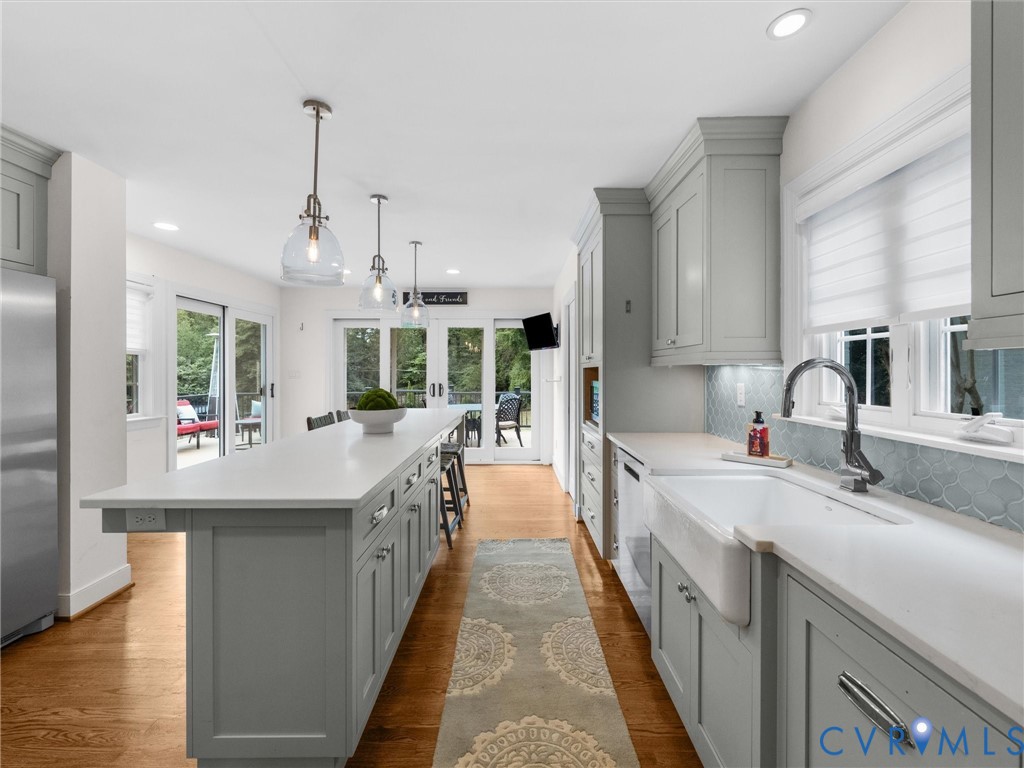 Kitchen featuring light gray cabinetry, a white farmhouse sink, light-toned countertops, hardwood flooring, and glass-paned doors
