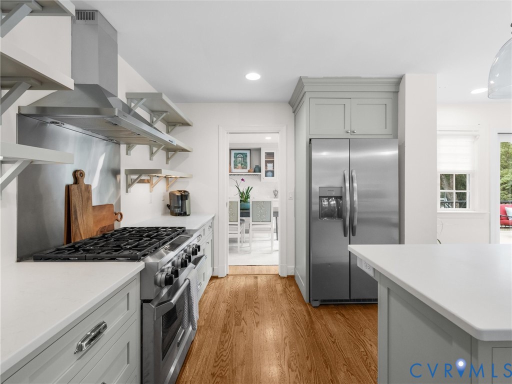 Wood-finish flooring, stainless steel appliances, stone countertops, light gray cabinetry, and a stainless steel range hood