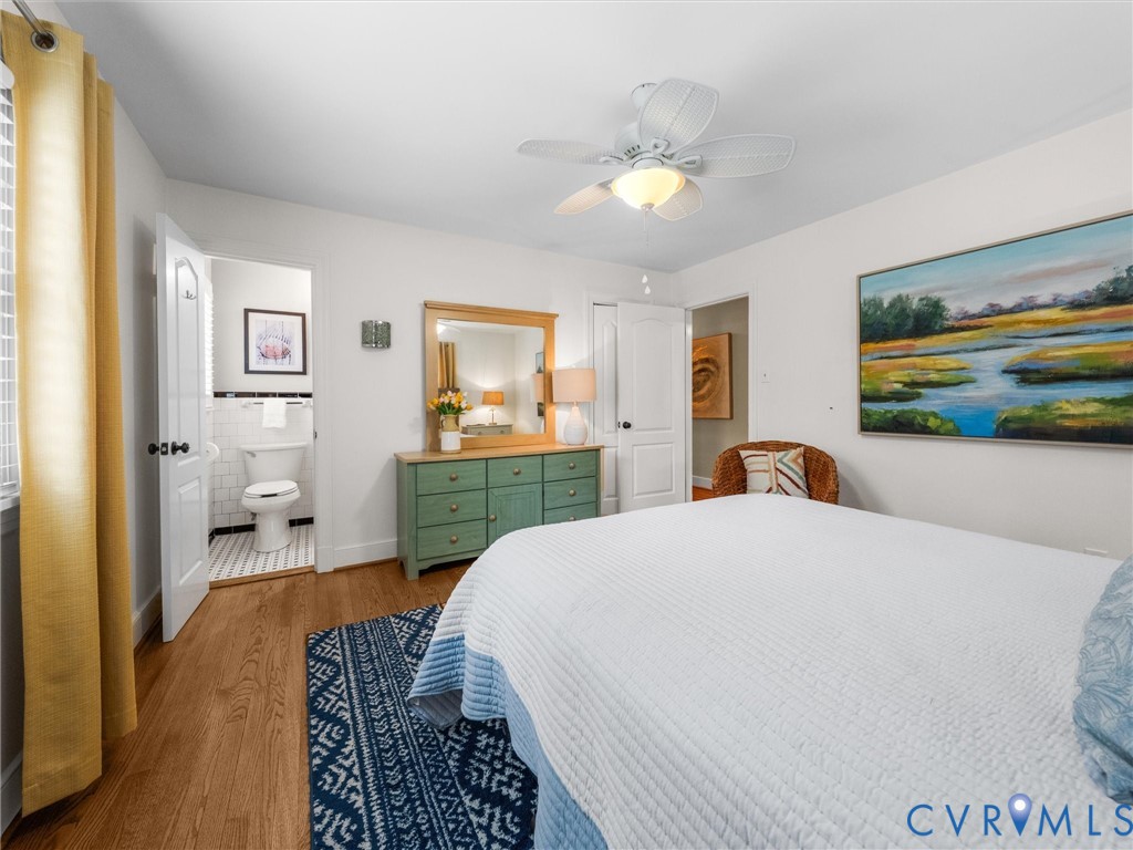Spacious primary bedroom with wood-finish flooring, ceiling fan with integrated lighting, and a green-painted dresser with mirror