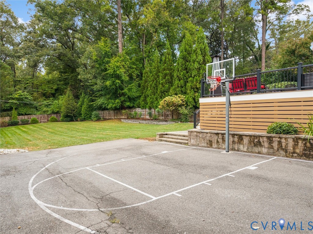 Paved sport court with basketball hoop, adjacent to a flat, manicured lawn