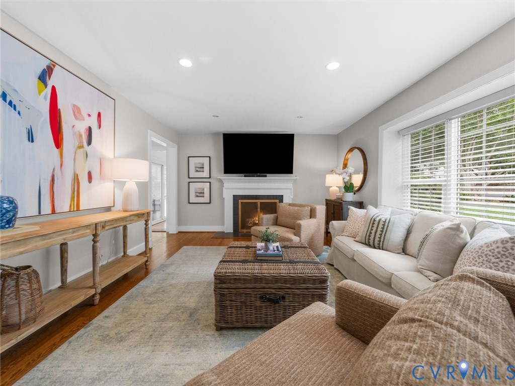 Hardwood flooring, recessed lighting, white fireplace with mantle, large windows with blinds