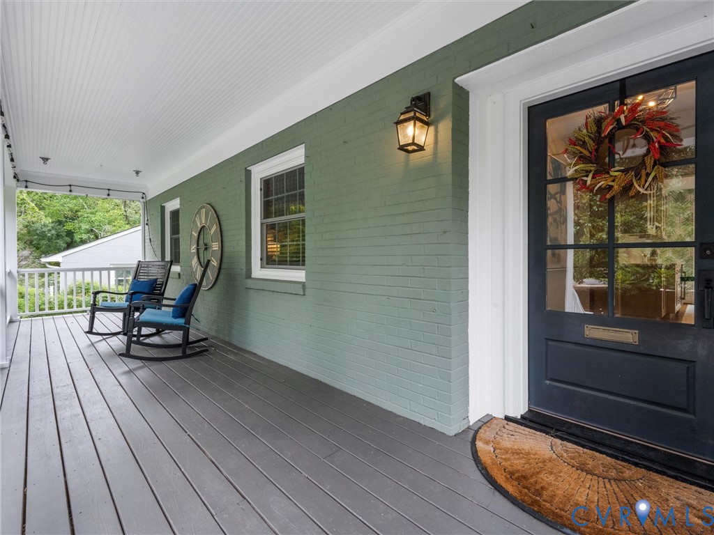 Covered porch with painted wood flooring, brick exterior, beadboard ceiling, and a glass-paneled entry door