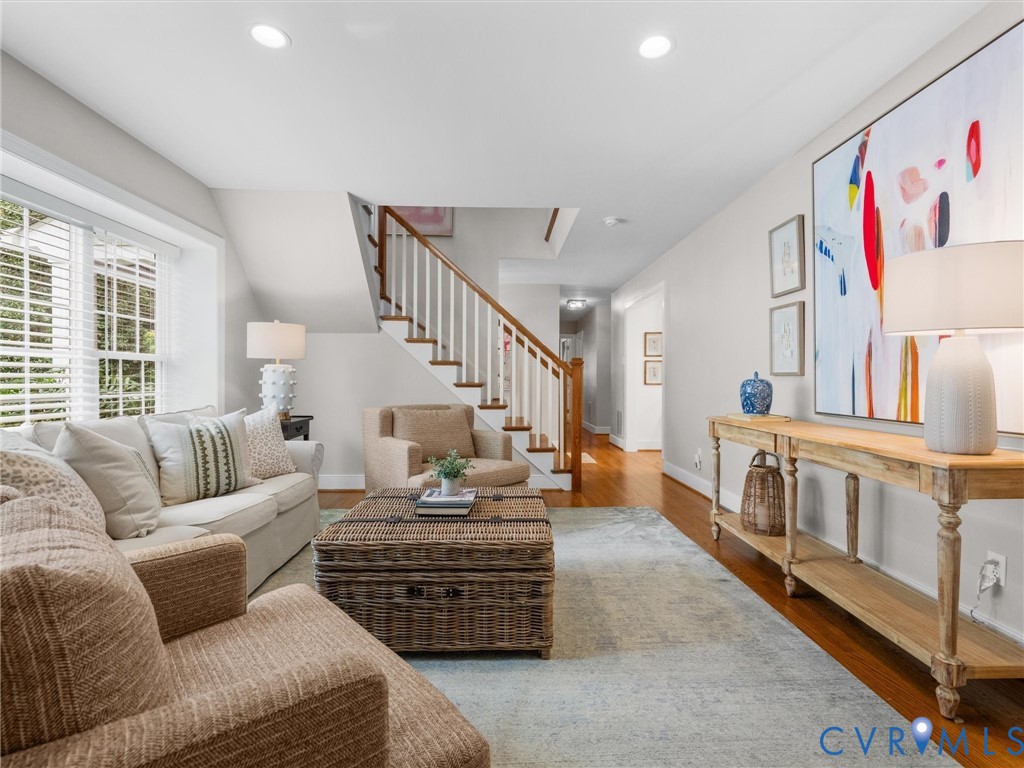 Recessed lighting, wood-finish flooring, staircase with wood handrail and white balusters, and a console table with lower shelf