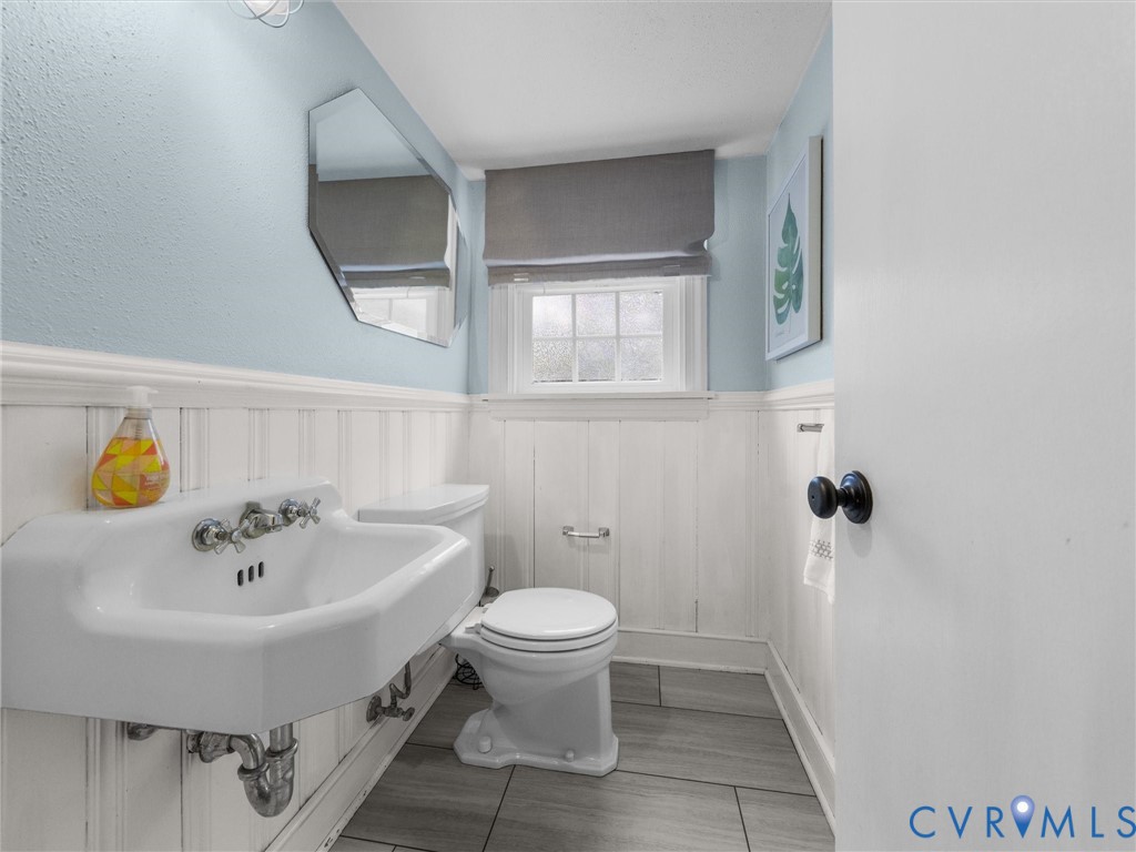 White wall-mounted sink with chrome fixtures, white wainscoting, and gray tile flooring