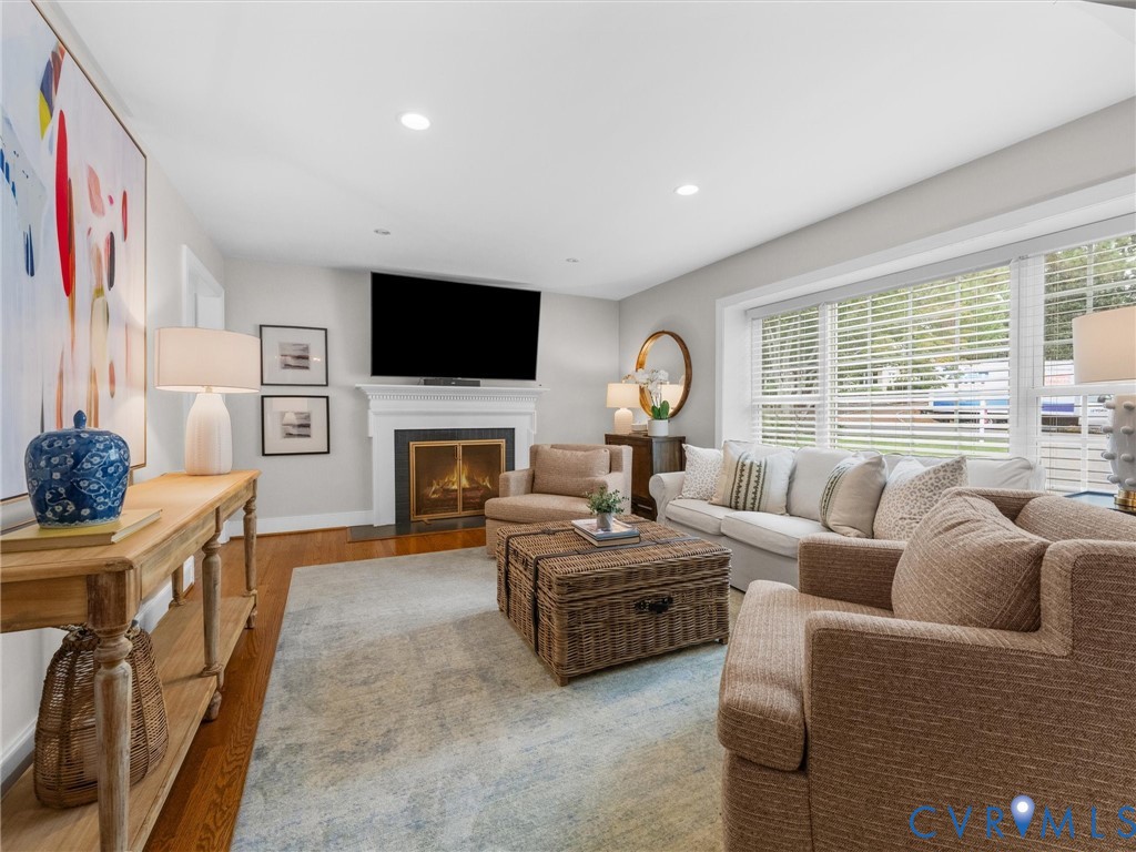 Hardwood flooring, fireplace with a classic white mantel, large windows with blinds, and recessed lighting