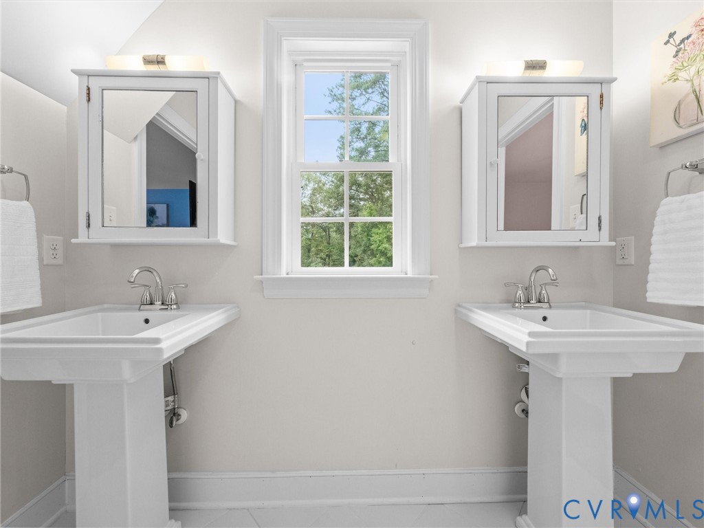 Two pedestal sinks with chrome fixtures, framed window, two mirrored medicine cabinets, and wall-mounted lighting