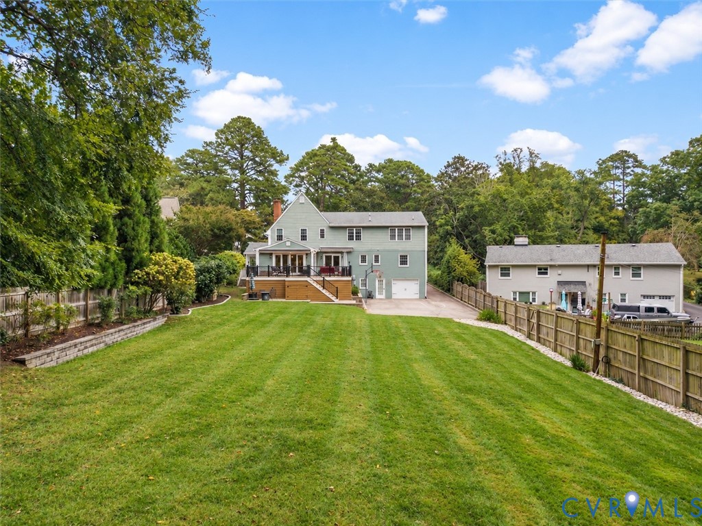 Expansive rear lawn with mature perimeter trees, a stone retaining wall, and a raised wooden deck with railings