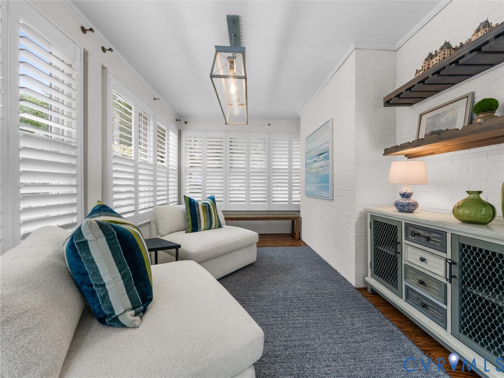 White plank shuttered windows, recessed ceiling, wood-finish flooring, white painted brick wall, and a linear pendant light fixture