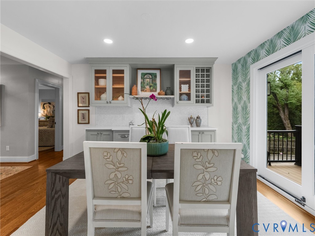 Built-in cabinetry with glass-front uppers and a tiled backsplash, recessed lighting, wood-finish flooring, and a sliding glass door leading to a balcony with black railings