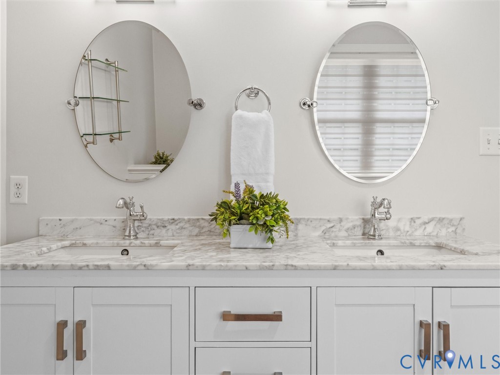 Dual oval mirrors, white shaker-style cabinetry, double undermount sinks, and stone countertops