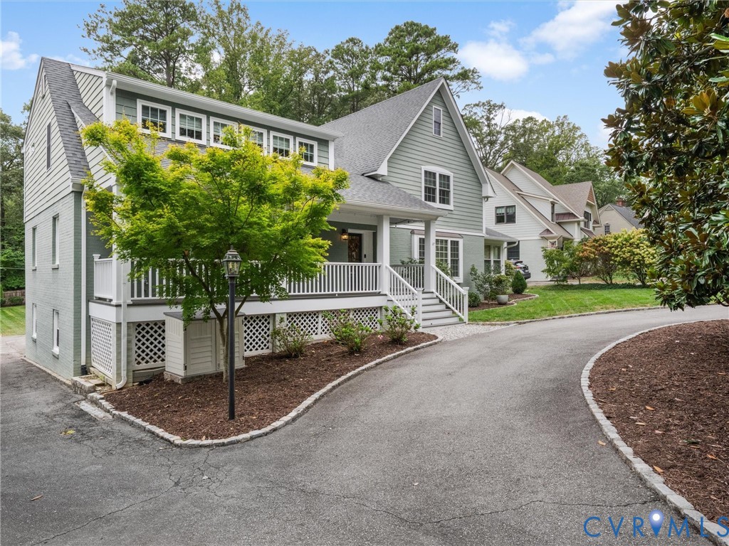 Light green siding exterior with a pitched roof, front porch with white railings, and a paved driveway