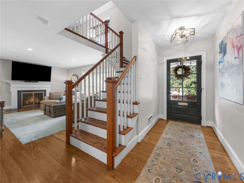Hardwood flooring throughout, a traditional fireplace with a white mantel, and a dark paneled front door with multiple glass panes