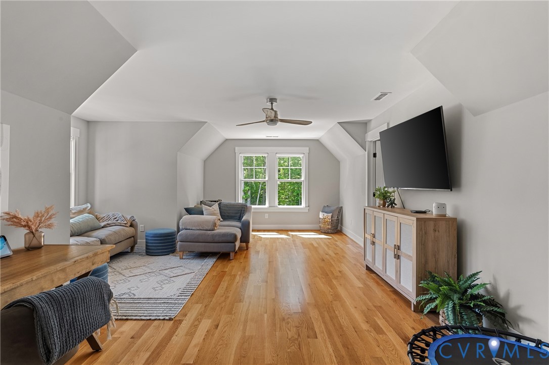 Expansive room featuring light wood-finish flooring, multiple windows, a ceiling fan, and sloped ceiling details