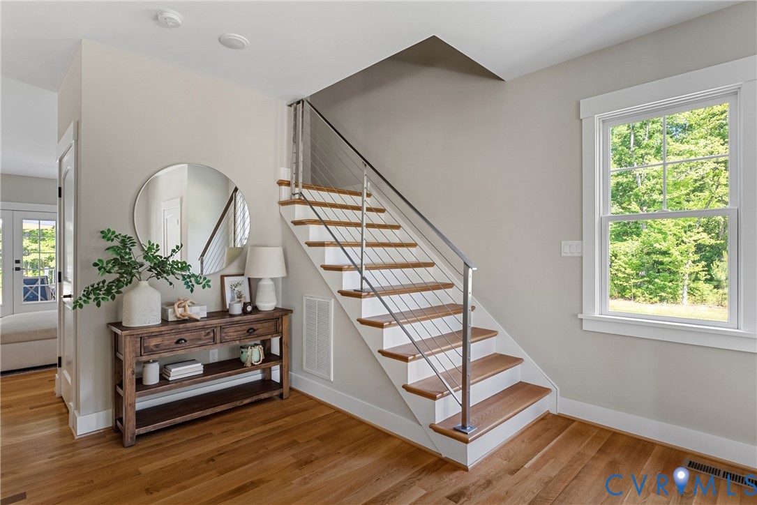Hardwood flooring extending to staircase treads, modern cable railing system, white window trim, and recessed lighting