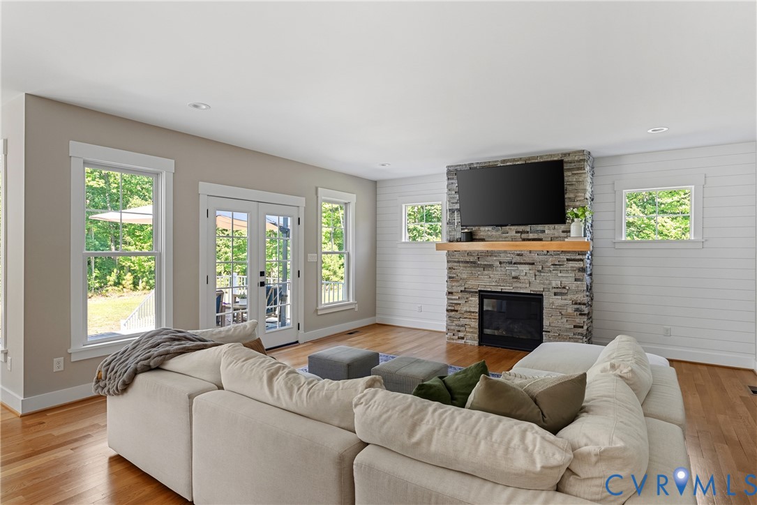 Living area featuring wood-finish flooring, a stone-clad fireplace with a wood mantle, and bright recessed lighting