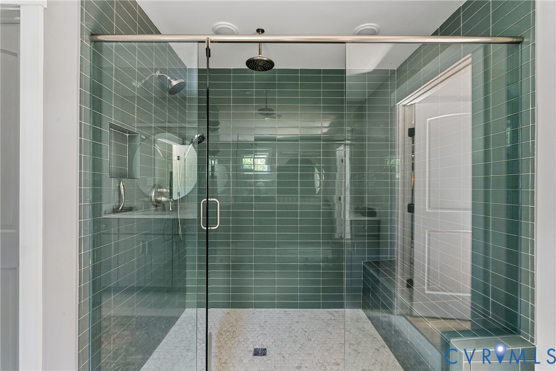 Glass-enclosed shower featuring a rain showerhead, a wall-mounted showerhead, and subway tile walls