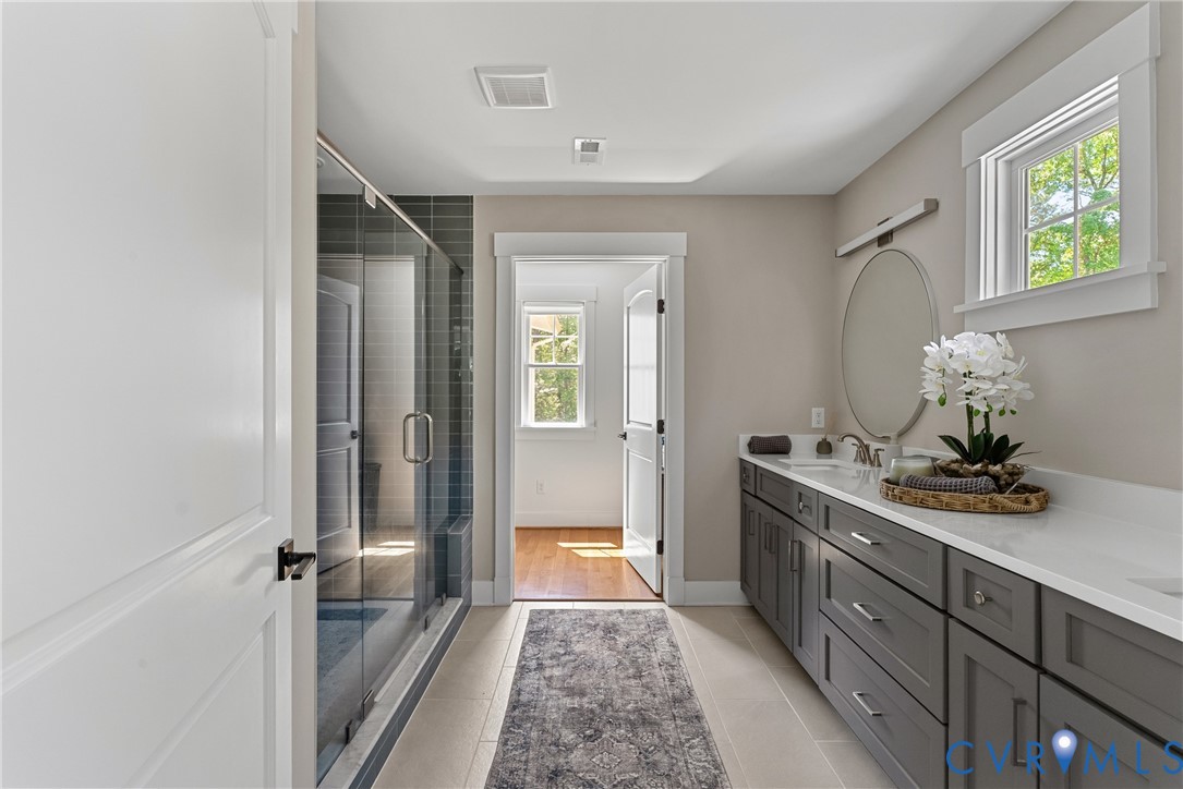 Spacious bathroom featuring a double vanity with stone countertops, a large walk-in shower with glass enclosure, and tile flooring