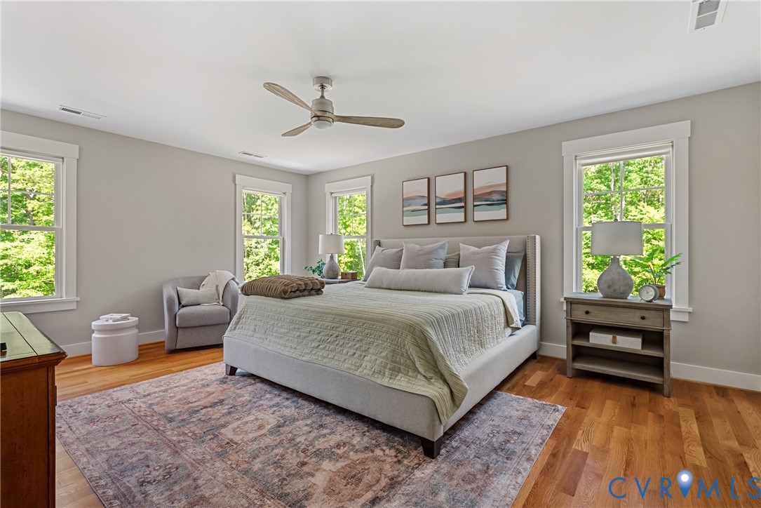 Hardwood flooring, multiple windows with white trim, a ceiling fan, and light gray wall paint