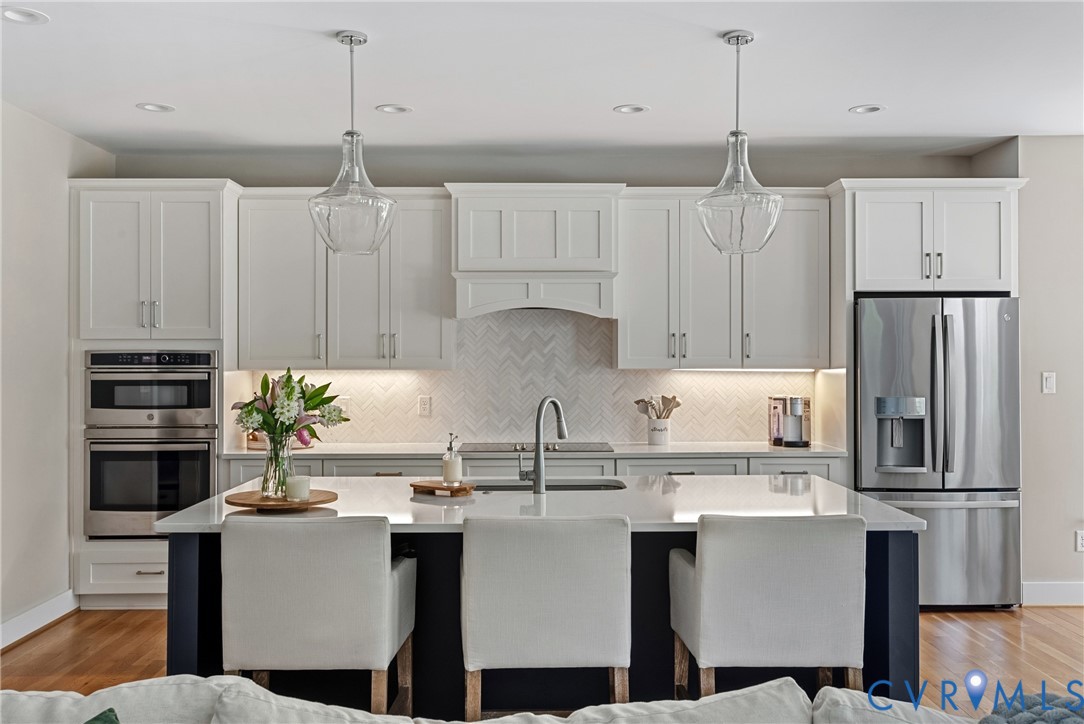 Spacious kitchen featuring white cabinetry, a built-in double oven, stainless steel French door refrigerator, large center island with seating, and wood-finish flooring