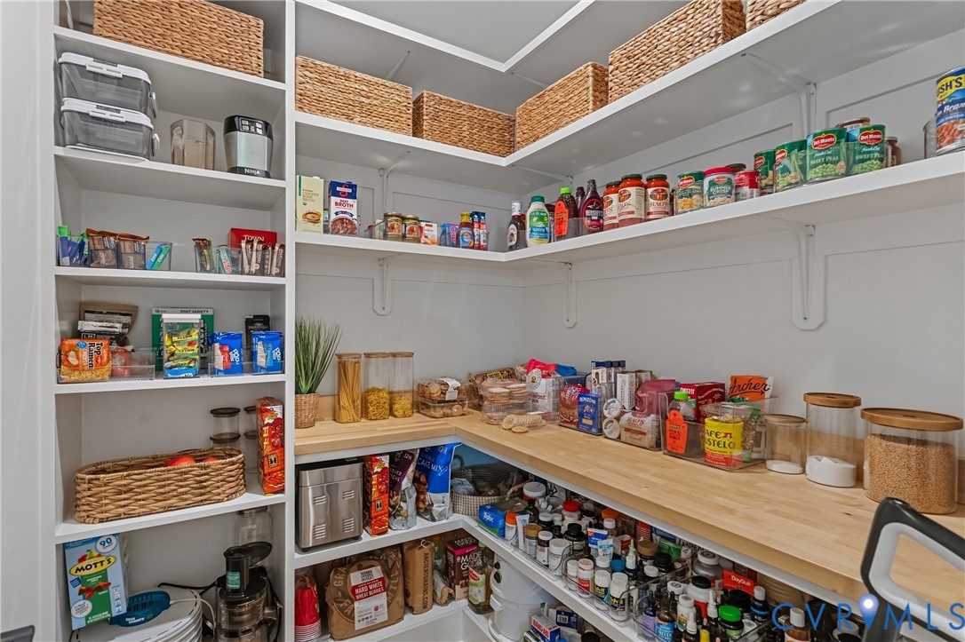 Custom storage pantry featuring white shelving, a wood-finish countertop, and built-in vertical storage