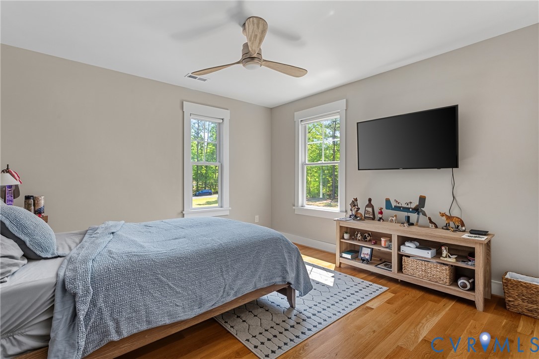 Hardwood flooring, two windows with white trim, a ceiling fan, and neutral wall paint