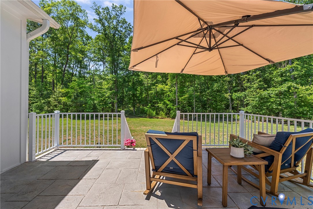 Patio featuring paver flooring, white railing, and a background of mature trees
