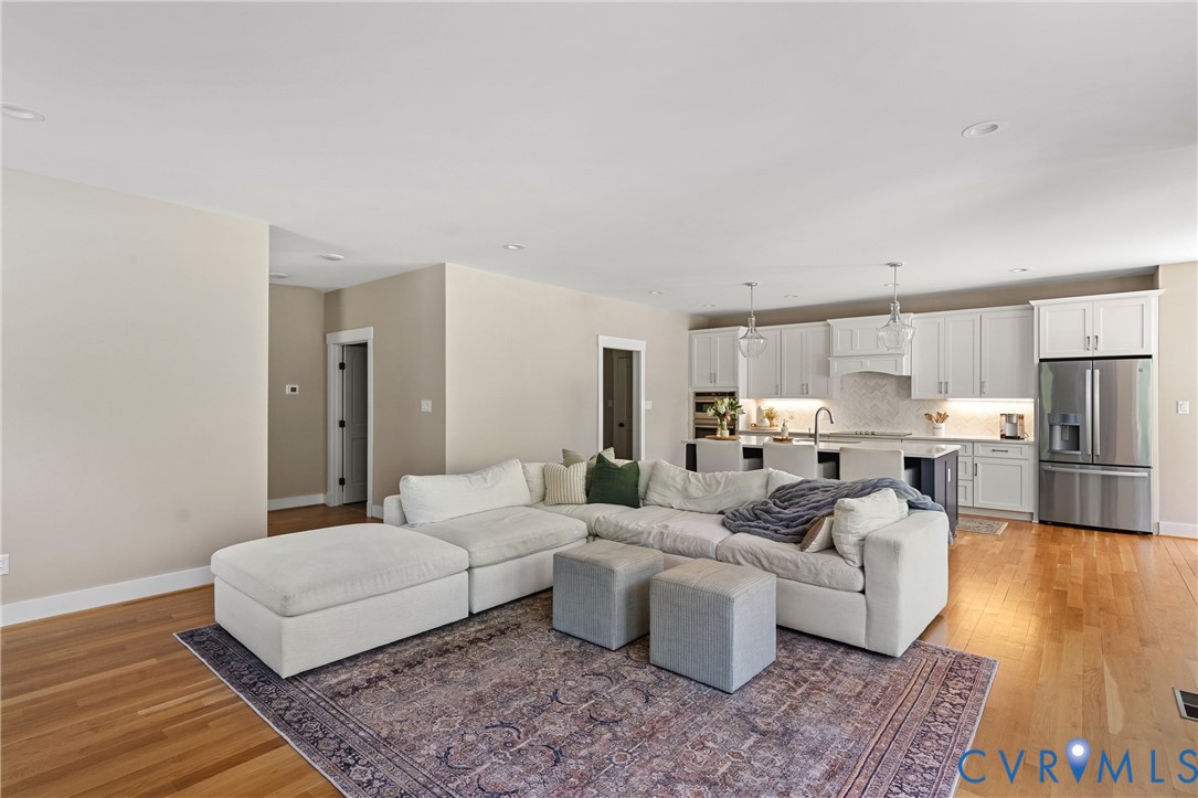 Hardwood flooring throughout, recessed lighting, and a kitchen featuring white cabinetry, stainless steel appliances, and a central island with pendant lighting