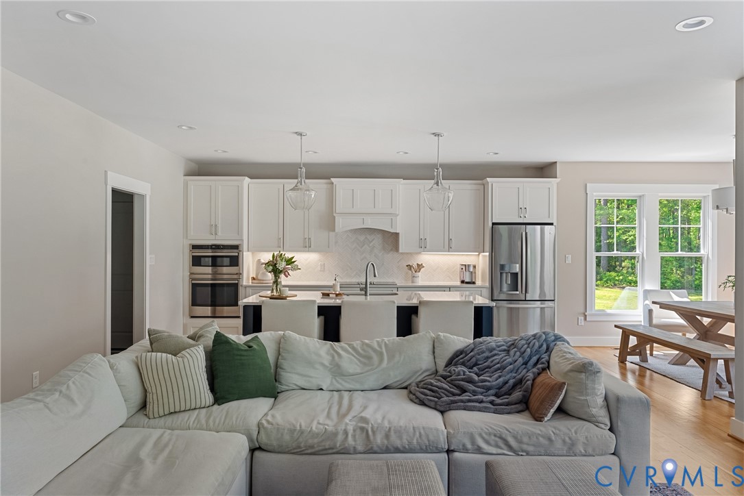 Open-concept living area featuring recessed lighting, wood-finish flooring, a kitchen island with pendant lighting, white cabinetry, and stainless steel appliances
