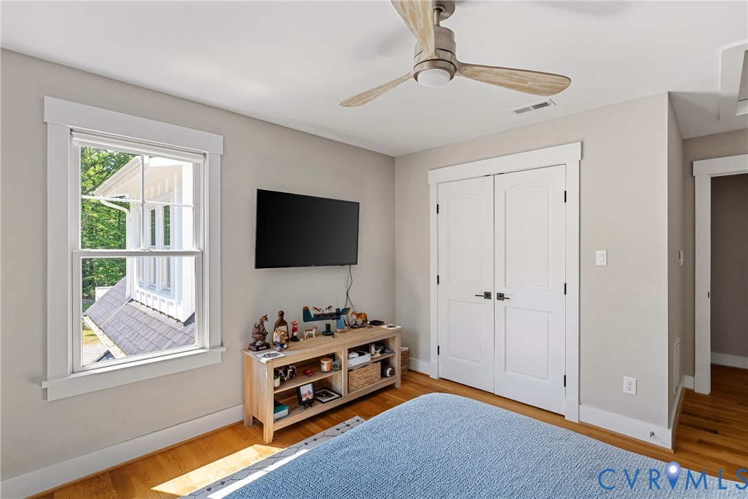 Hardwood flooring, bright window with white trim, built-in double-door closet, and a ceiling fan with light fixture