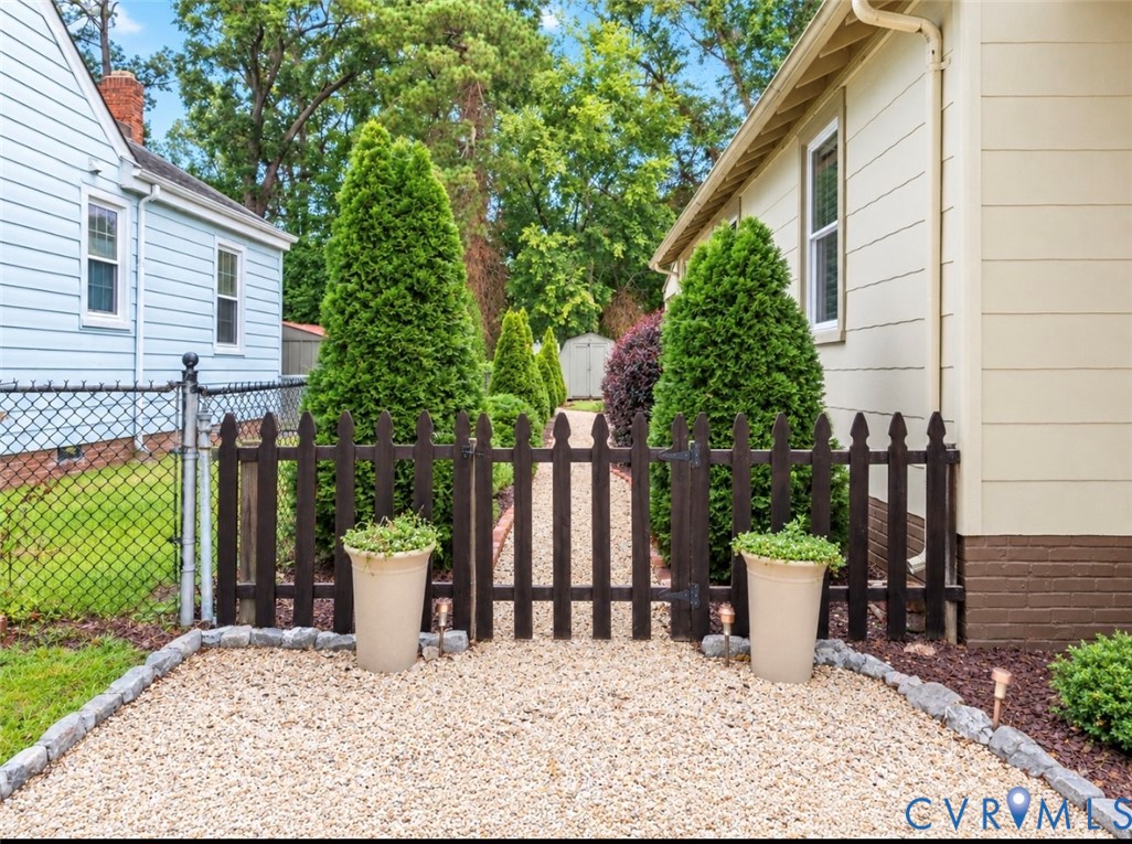 Gravel pathway with a dark wood picket fence, chain link fencing, and established conical shrubs