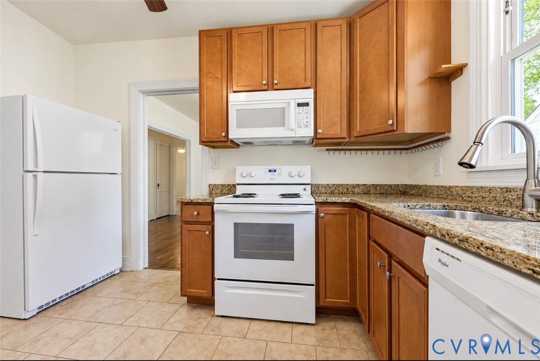 Kitchen featuring wood cabinetry, stone countertops, stainless steel sink with gooseneck faucet, white appliances, and tile flooring