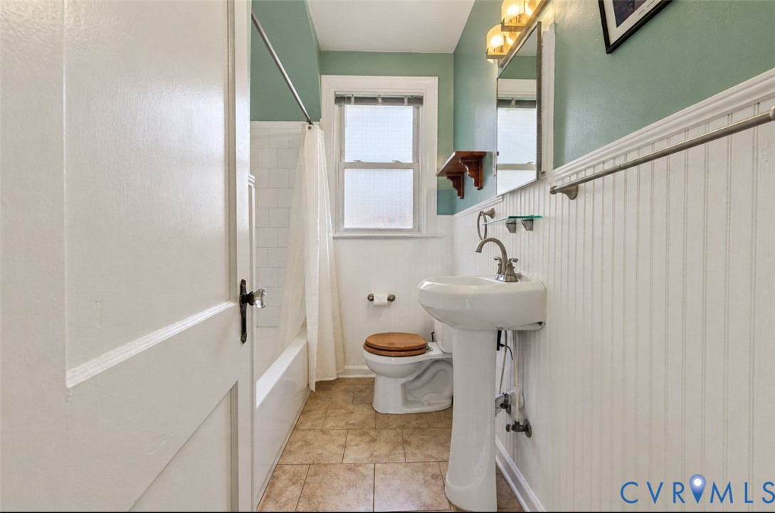 Pedestal sink with brushed nickel faucet, wall-mounted mirror, beadboard wainscoting, tiled flooring, and window with privacy glass