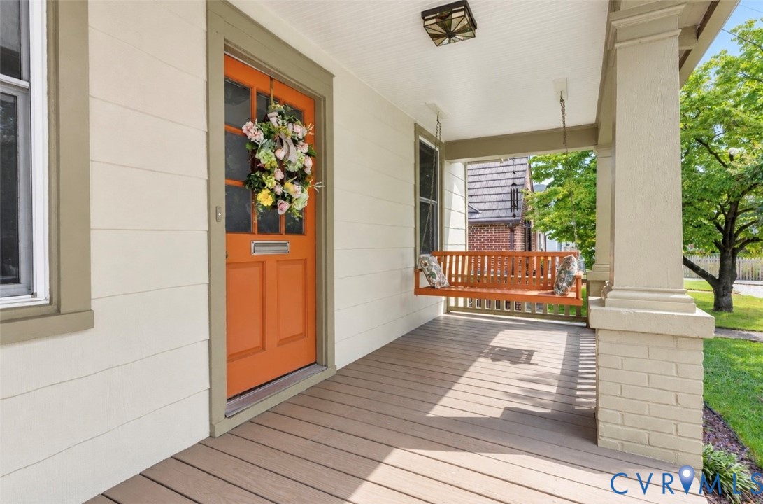 Covered front porch featuring wood decking, detailed front door with transom window, and brick based columns