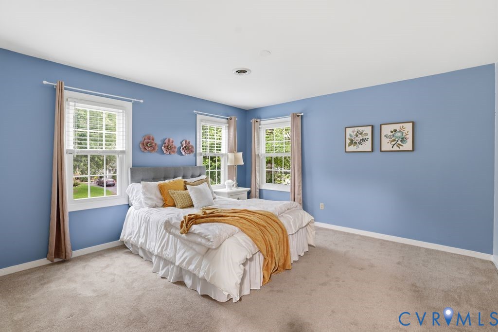 Bedroom featuring two windows with white blinds, light blue walls, and neutral carpet flooring