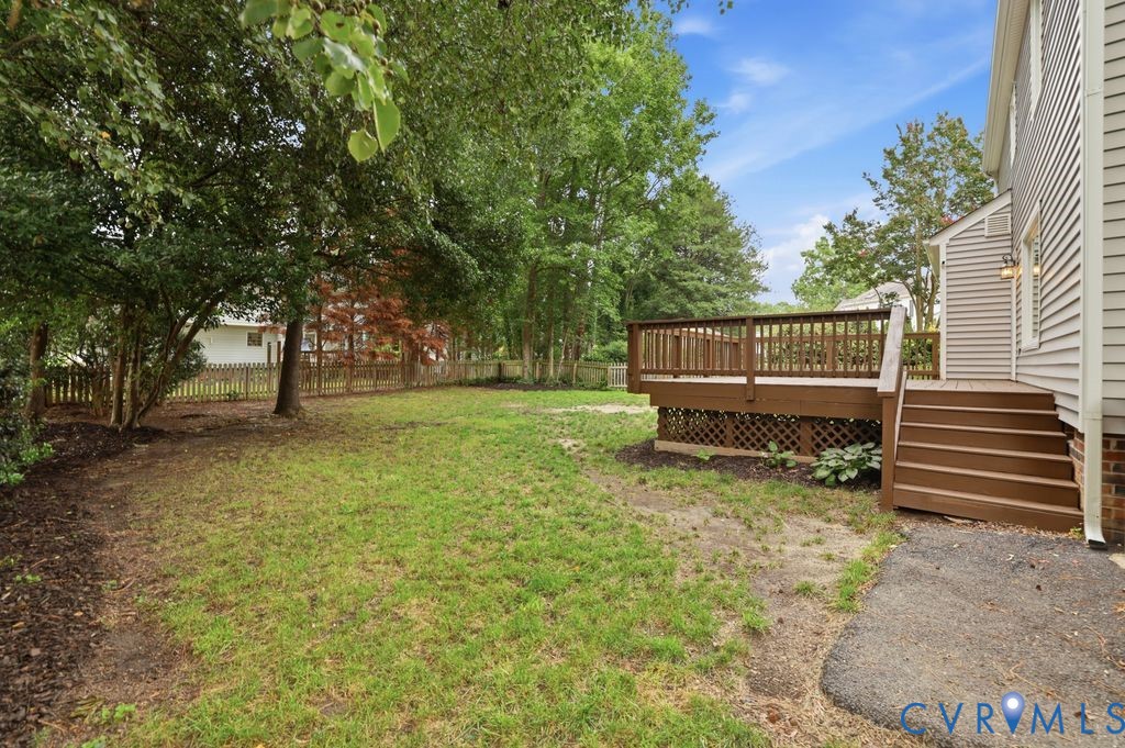 Spacious backyard featuring a large elevated wood deck with railing and steps, mature trees, and a partial wood fence