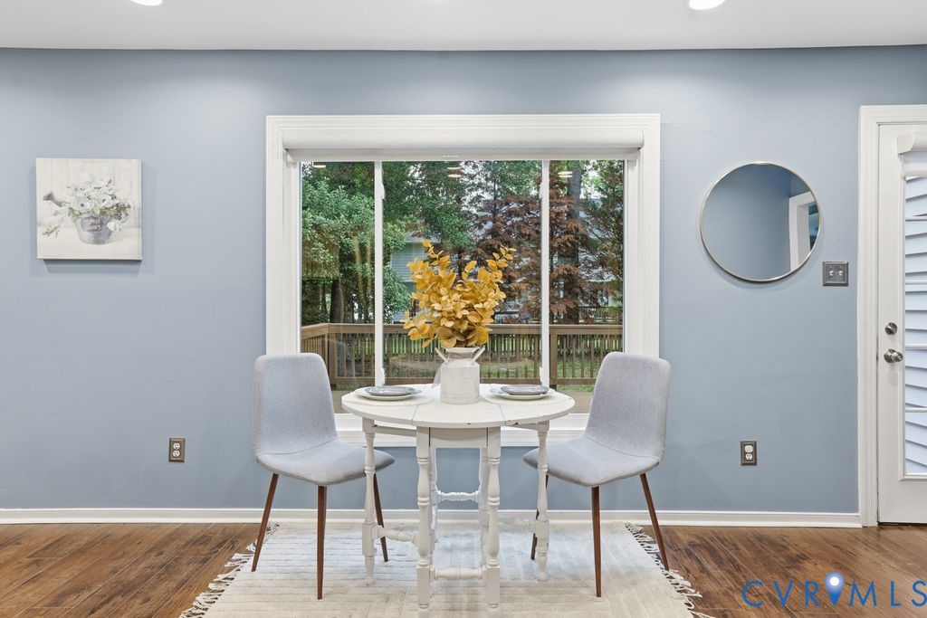 Dining area featuring a full-light window with white trim, wood-finish flooring, and a white paneled door with louvered blinds
