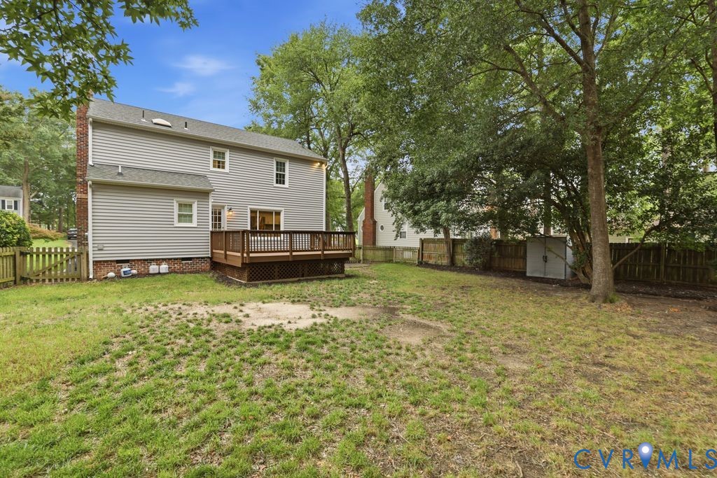 Rear exterior featuring a spacious wood deck, gray horizontal siding, a brick chimney, and a fenced backyard with mature trees