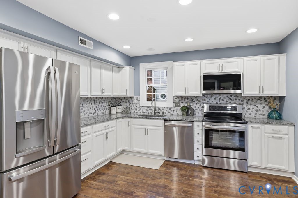 Kitchen featuring stainless steel appliances, white cabinetry, granite countertops, a decorative tile backsplash, and wood-finish flooring