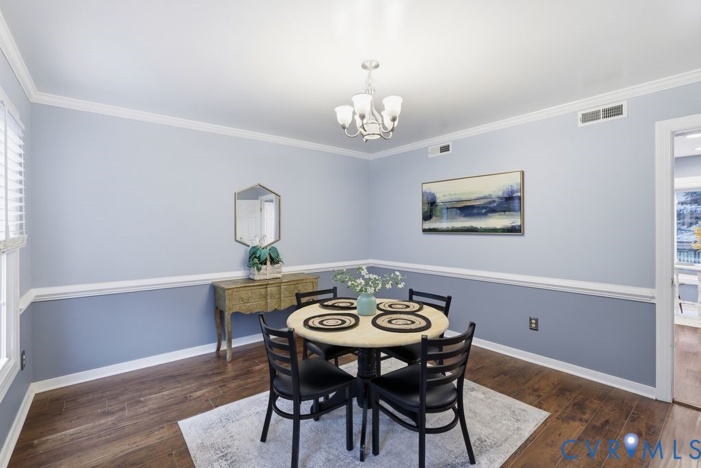 Dining area featuring wood-finish flooring, two-tone painted walls with chair rail molding, and a chandelier with white glass shades