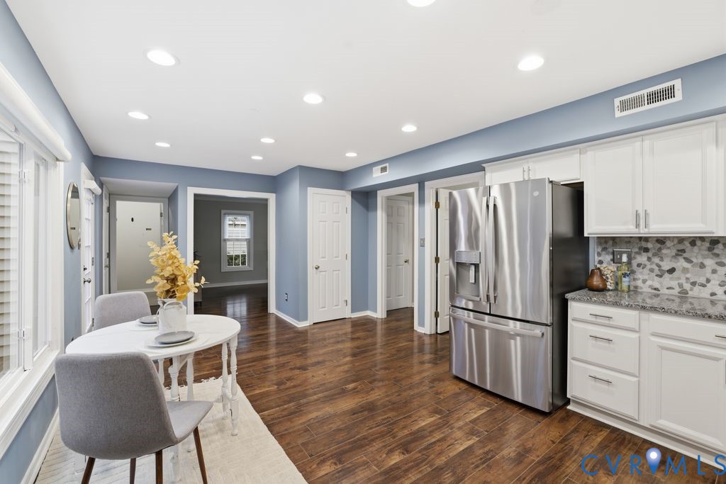 Modern kitchen and dining area featuring stainless steel French-door refrigerator, white cabinetry with soft-close drawers, mosaic tile backsplash, and integrated appliances