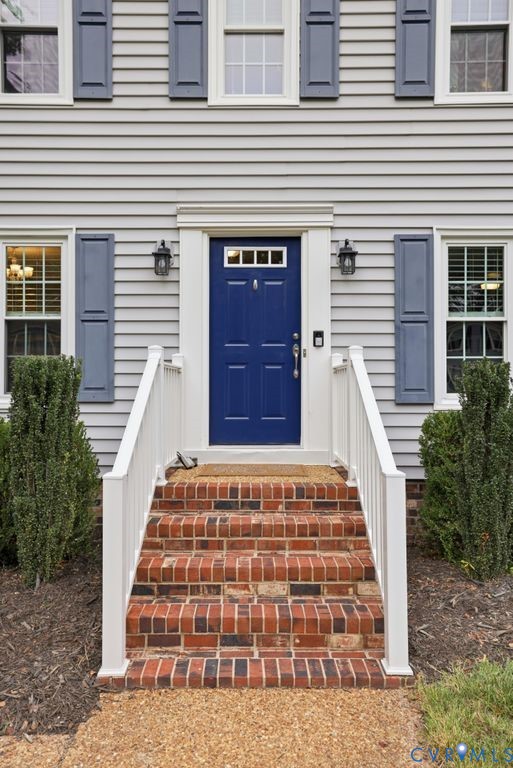 Classic Colonial entrance featuring a navy blue six-panel front door with brass hardware, flanked by symmetrical blue shutters and white trim