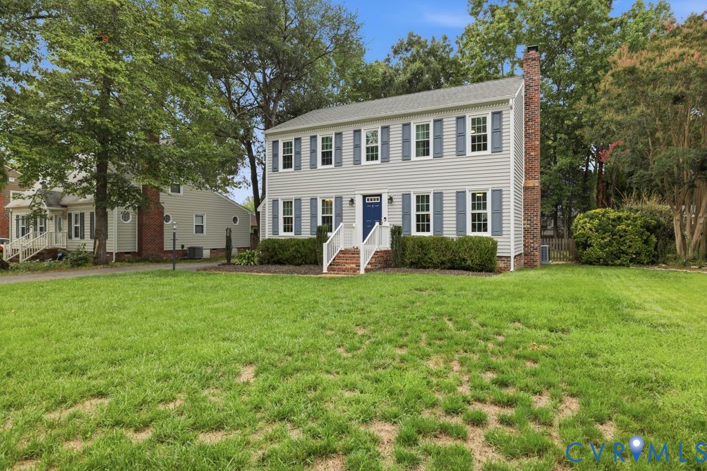 Two-story colonial residence featuring light gray siding, a prominent brick chimney, and blue window shutters