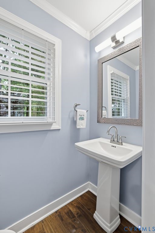 Pedestal sink with chrome faucet, wood-finish flooring, light blue wall paint, white trim, and a window featuring white blinds