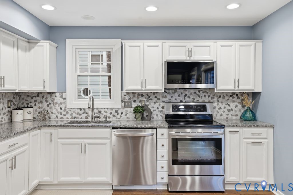 Kitchen featuring white shaker-style cabinetry, stainless steel appliances, speckled stone countertops, and a full-height mosaic tile backsplash