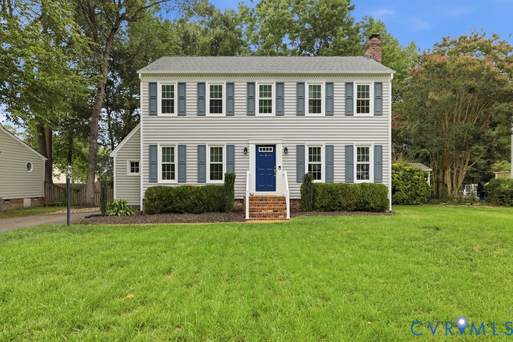 Two-story colonial-style residence featuring light gray siding, dark blue shutters, a prominent blue front door, and a brick chimney