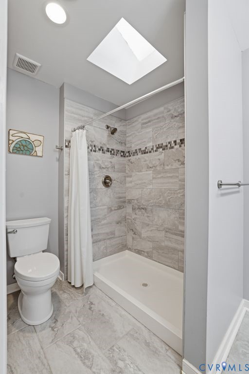 Bathroom featuring a skylight, walk-in shower with tiled walls and decorative mosaic accent, white shower pan, and coordinating tile flooring