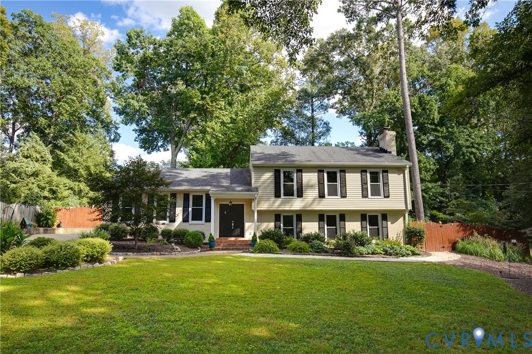 Two-story siding exterior with dark shutters, established landscaping, mature trees, and a front lawn