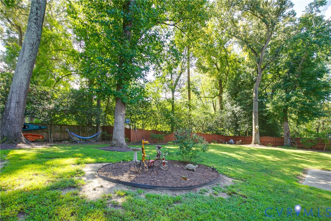 Expansive backyard with a manicured lawn, mature trees, and a wooden privacy fence
