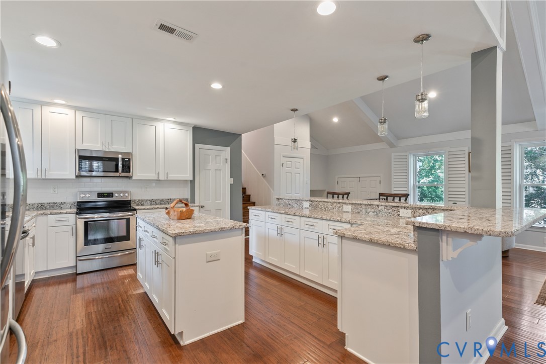 Kitchen featuring stainless steel appliances, white cabinetry, a central island, and stone countertops
